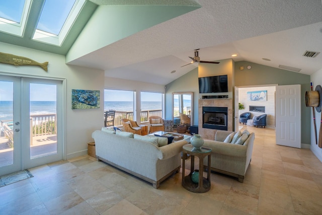 living room featuring french doors, a textured ceiling, lofted ceiling with skylight, ceiling fan, and a tile fireplace