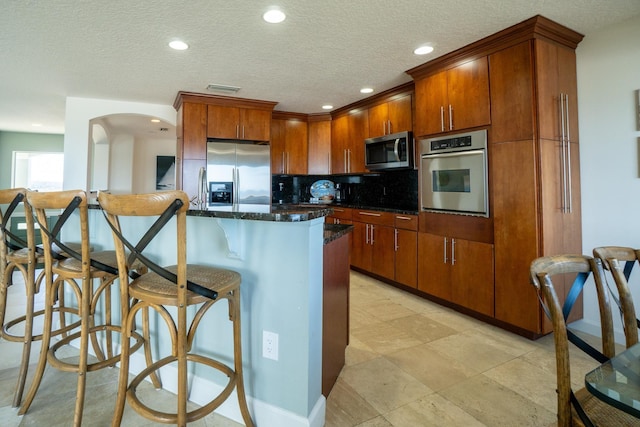 kitchen featuring backsplash, dark stone counters, a textured ceiling, and appliances with stainless steel finishes