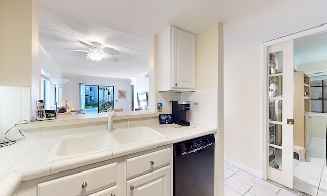  - kitchen featuring dishwasher, a sink, tasteful backsplash, tile counters, and white cabinetry