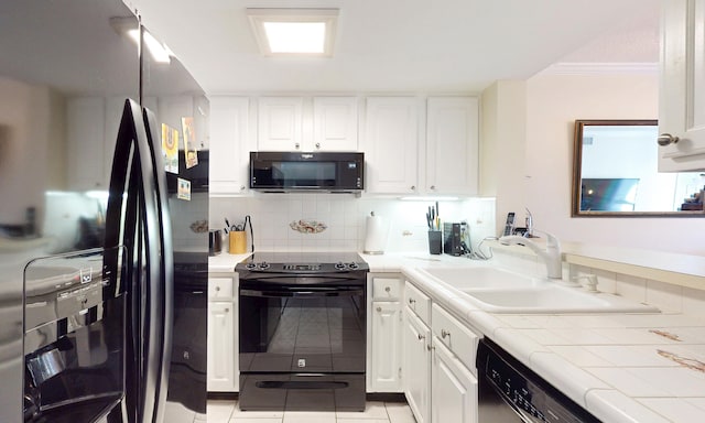  - kitchen with black appliances, tile counters, light tile patterned floors, white cabinets, and crown molding