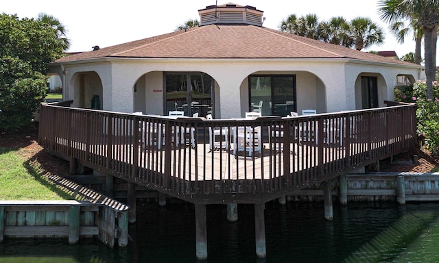  - back of house featuring stucco siding, a deck with water view, a chimney, and roof with shingles
