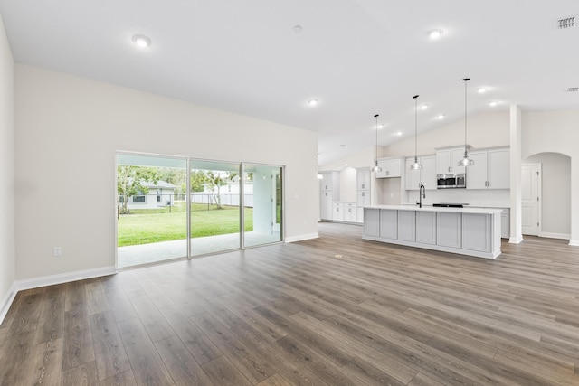 unfurnished living room featuring arched walkways, high vaulted ceiling, wood finished floors, and a sink