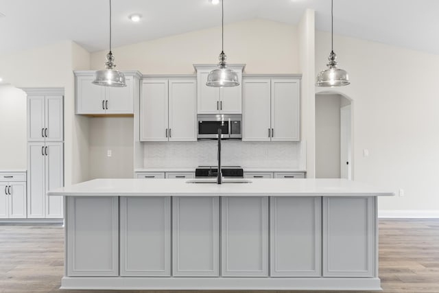 kitchen featuring a center island with sink, a sink, stainless steel microwave, light wood finished floors, and light countertops