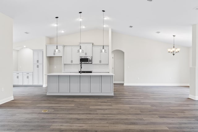 kitchen featuring stainless steel microwave, a center island with sink, light countertops, arched walkways, and high vaulted ceiling