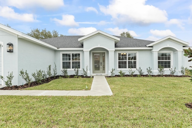 ranch-style house featuring stucco siding, roof with shingles, and a front yard