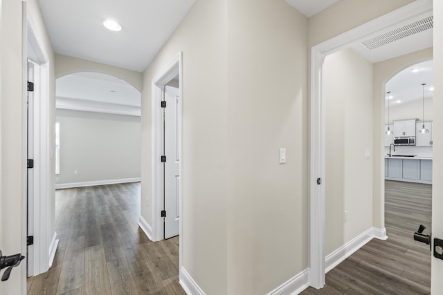 hallway featuring visible vents, arched walkways, dark wood-style flooring, and baseboards