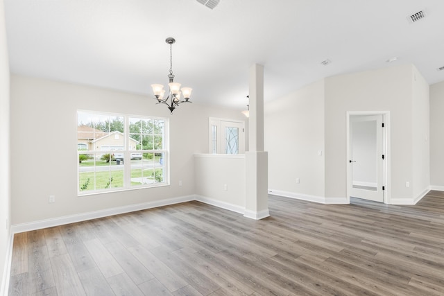 empty room with visible vents, baseboards, a notable chandelier, and wood finished floors