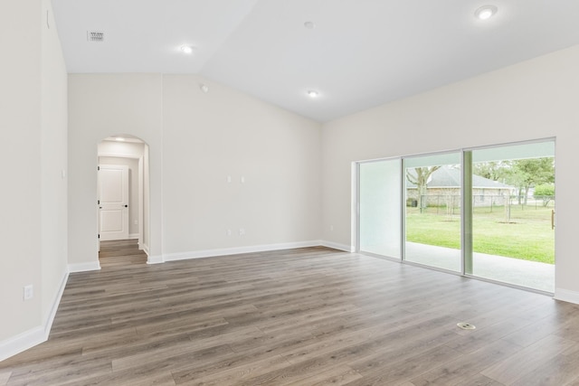 spare room with visible vents, wood finished floors, arched walkways, baseboards, and vaulted ceiling