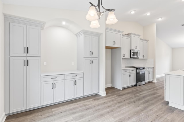 kitchen with light wood-type flooring, an inviting chandelier, appliances with stainless steel finishes, light countertops, and vaulted ceiling