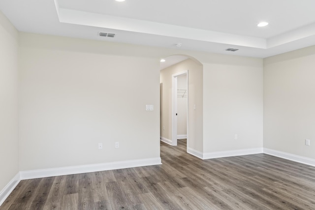 unfurnished room with visible vents, a raised ceiling, baseboards, and wood finished floors