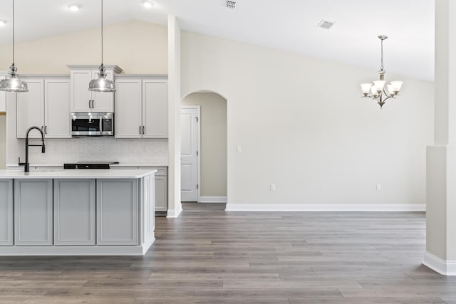 kitchen featuring stainless steel microwave, backsplash, light countertops, arched walkways, and a sink