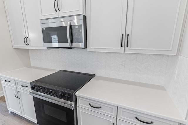 kitchen featuring light countertops, range with electric stovetop, white cabinetry, stainless steel microwave, and tasteful backsplash