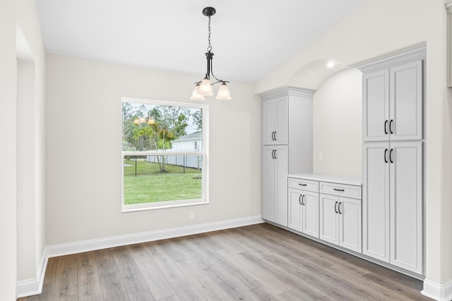 unfurnished dining area with light wood-type flooring, baseboards, and an inviting chandelier