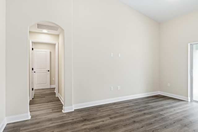 unfurnished room with arched walkways, visible vents, dark wood-type flooring, and baseboards