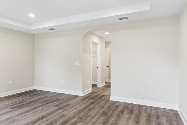 spare room featuring visible vents, wood finished floors, baseboards, and arched walkways