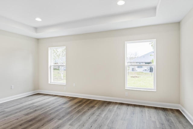 spare room featuring recessed lighting, a raised ceiling, baseboards, and wood finished floors