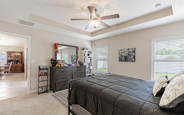 bedroom with ceiling fan, light colored carpet, a textured ceiling, and a tray ceiling