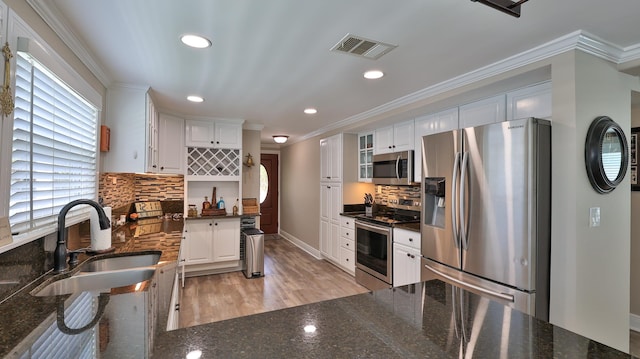 kitchen with appliances with stainless steel finishes, light hardwood / wood-style floors, white cabinetry, and crown molding