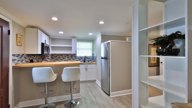 kitchen featuring wooden counters, a kitchen breakfast bar, appliances with stainless steel finishes, ornamental molding, and white cabinets