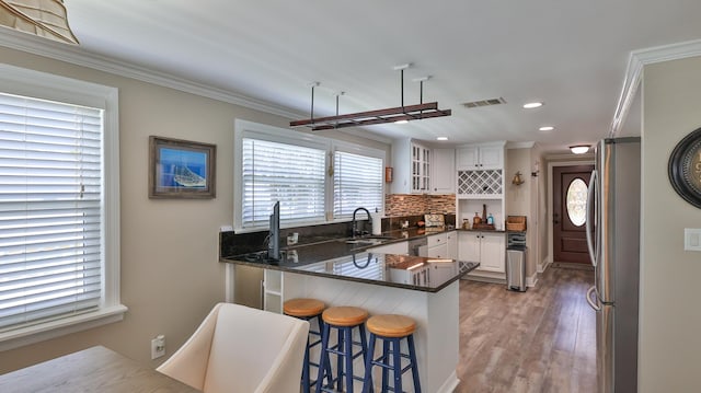 kitchen with kitchen peninsula, light hardwood / wood-style flooring, appliances with stainless steel finishes, white cabinetry, and a breakfast bar area