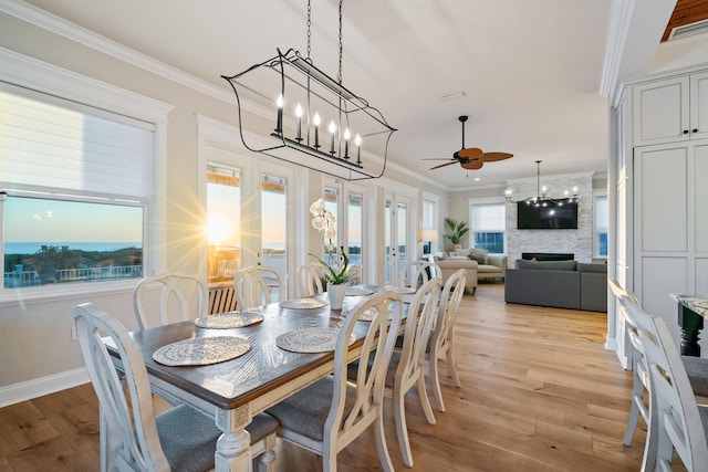 dining room with crown molding, a fireplace, ceiling fan with notable chandelier, and light hardwood / wood-style flooring