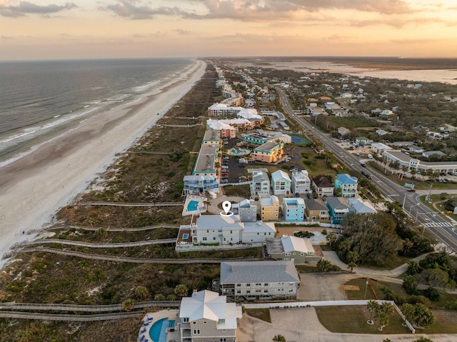 aerial view at dusk featuring a water view and a beach view