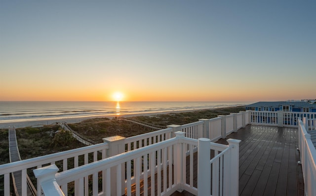 deck at dusk featuring a view of the beach and a water view