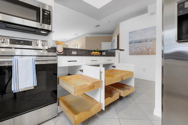 kitchen with dark stone counters, stainless steel appliances, crown molding, light tile patterned floors, and white cabinets