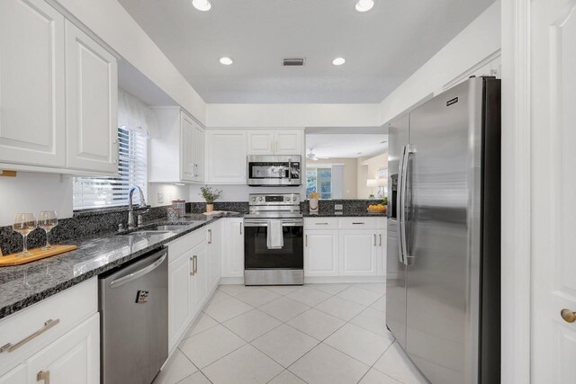 kitchen featuring sink, light tile patterned floors, dark stone countertops, white cabinets, and appliances with stainless steel finishes