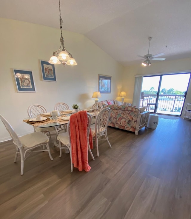 dining space with ceiling fan with notable chandelier, dark wood-type flooring, and vaulted ceiling