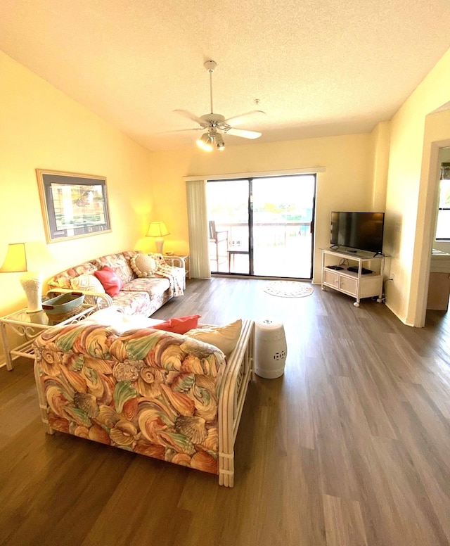 living room with lofted ceiling, ceiling fan, dark wood-type flooring, and a textured ceiling