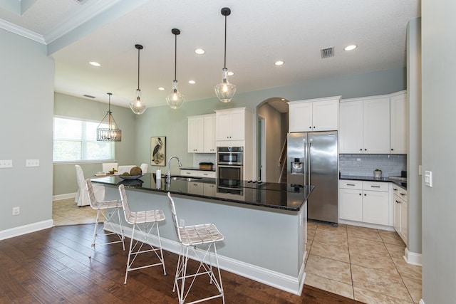 kitchen featuring white cabinetry, stainless steel appliances, an island with sink, and light hardwood / wood-style flooring