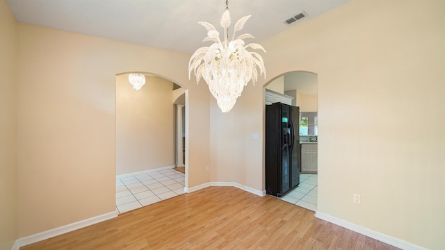 unfurnished room with visible vents, baseboards, arched walkways, light wood finished floors, and a notable chandelier
