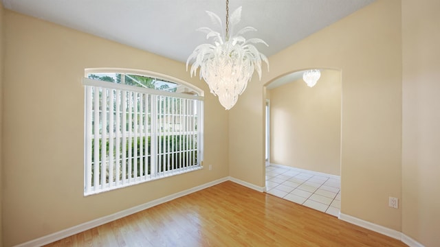 spare room with arched walkways, a chandelier, wood finished floors, and lofted ceiling