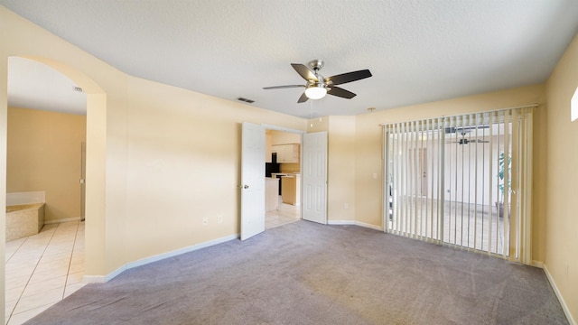 empty room with a ceiling fan, a textured ceiling, visible vents, arched walkways, and light tile patterned floors