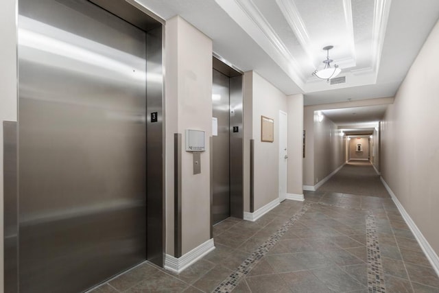 hall with visible vents, a raised ceiling, ornamental molding, elevator, and baseboards