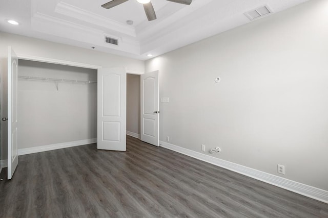 unfurnished bedroom featuring visible vents, a tray ceiling, dark wood-style floors, a closet, and baseboards