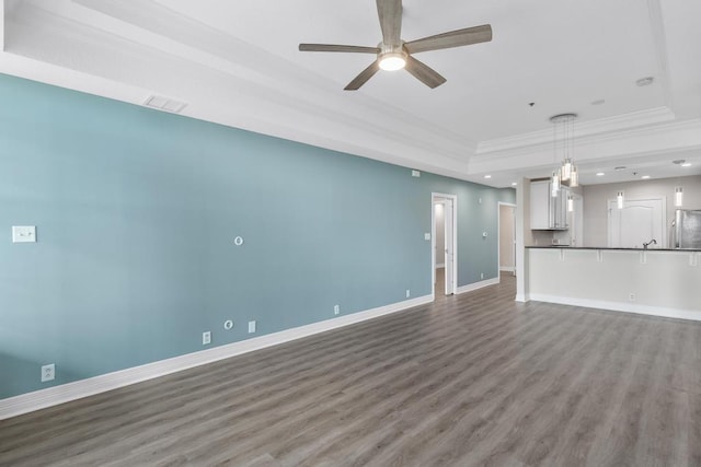 unfurnished living room featuring a raised ceiling, ornamental molding, a ceiling fan, wood finished floors, and baseboards