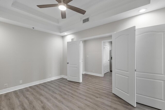 spare room with baseboards, visible vents, a tray ceiling, light wood-style flooring, and ceiling fan