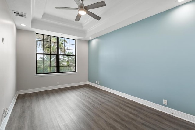 empty room with a ceiling fan, baseboards, visible vents, dark wood finished floors, and a tray ceiling