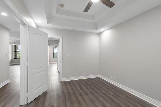 spare room with a tray ceiling, baseboards, ceiling fan, and dark wood-style flooring