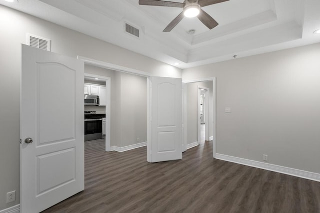 empty room featuring dark wood finished floors, visible vents, a raised ceiling, and ceiling fan