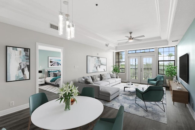 living room with a ceiling fan, visible vents, baseboards, a tray ceiling, and dark wood-style flooring