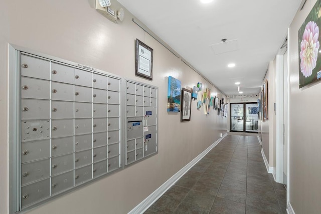 hallway with dark tile patterned floors, mail area, and baseboards