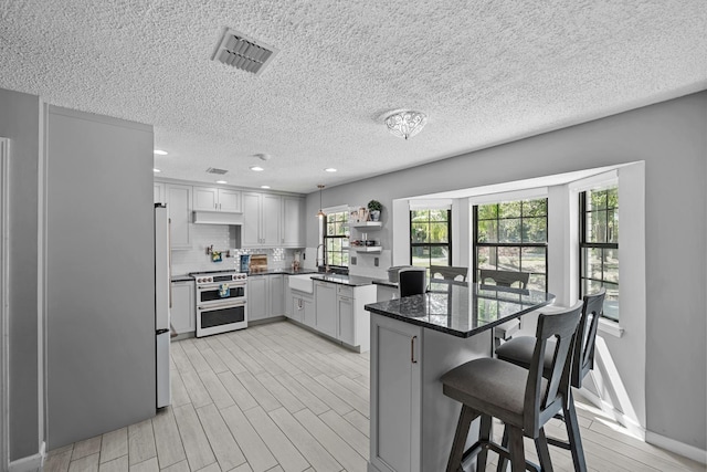 kitchen featuring a breakfast bar, dark stone counters, hanging light fixtures, stainless steel stove, and light hardwood / wood-style flooring