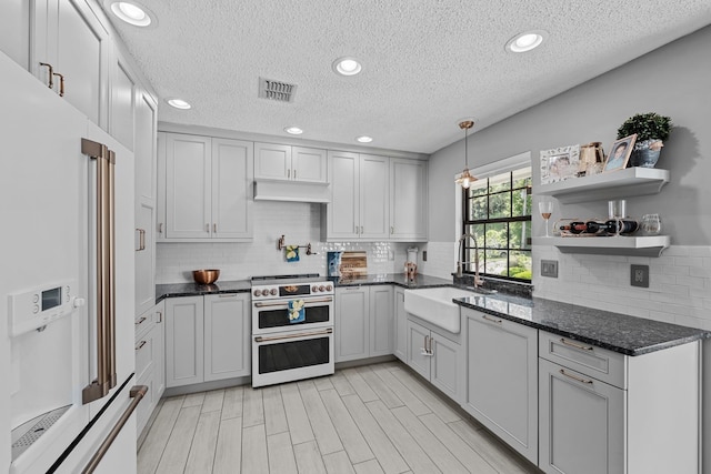 kitchen featuring sink, range with two ovens, white fridge with ice dispenser, dark stone countertops, and hanging light fixtures