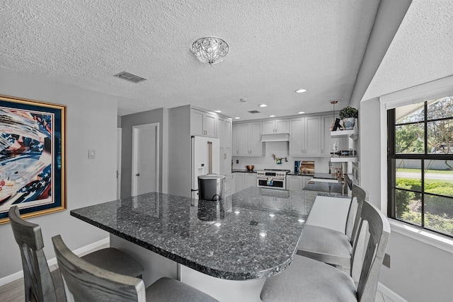 kitchen featuring hanging light fixtures, high end white fridge, a textured ceiling, stainless steel range, and white cabinetry