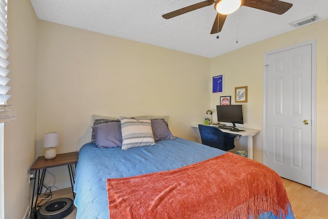 bedroom featuring a textured ceiling, light wood-style flooring, visible vents, baseboards, and a ceiling fan