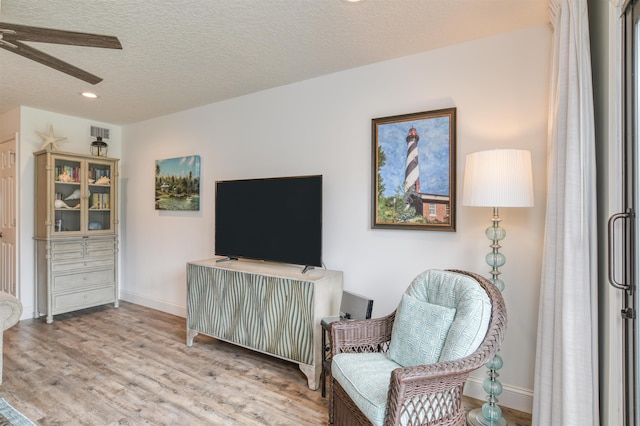 living area with a textured ceiling, light wood-type flooring, and ceiling fan