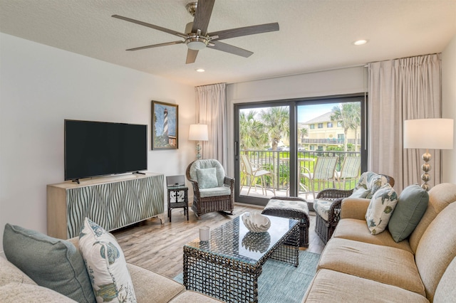 living room featuring ceiling fan, a textured ceiling, and light wood-type flooring